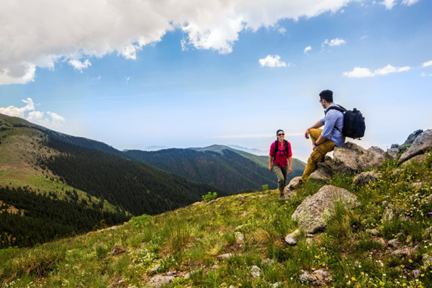 Two people hiking and surrounded by green, rolling mountains