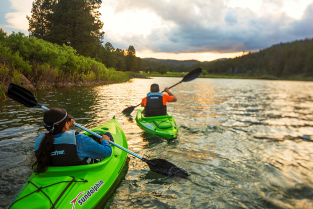 Two people in green kayaks paddling on a river during sunset